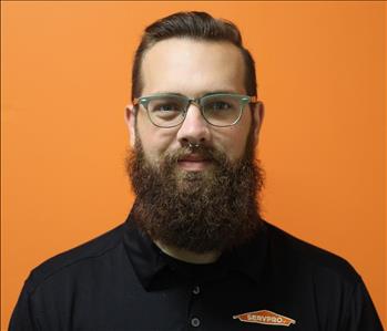 A man in a black shirt standing in front of an orange background