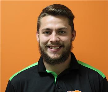 A man in a black shirt standing in front of an orange background