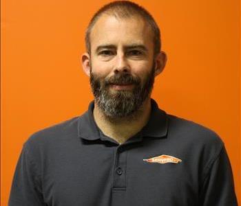 A man in a black shirt standing in front of an orange background