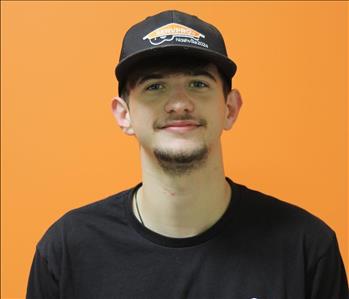 A man in a black shirt standing in front of an orange background