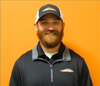 A man in a black shirt standing in front of an orange background