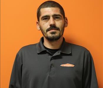 A man in a gray shirt standing in front of an orange background