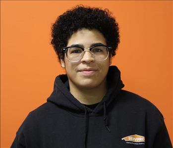 A woman in a black shirt standing in front of an orange background