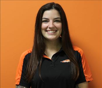 A woman in a black shirt standing in front of an orange background