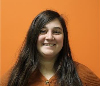 A woman in a brown shirt standing in front of an orange background