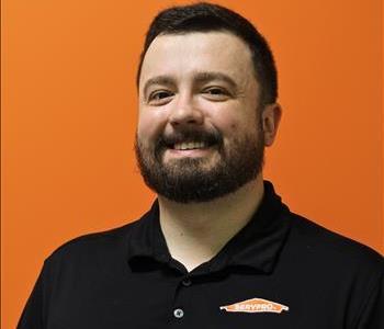 A man in a black shirt standing in front of an orange background